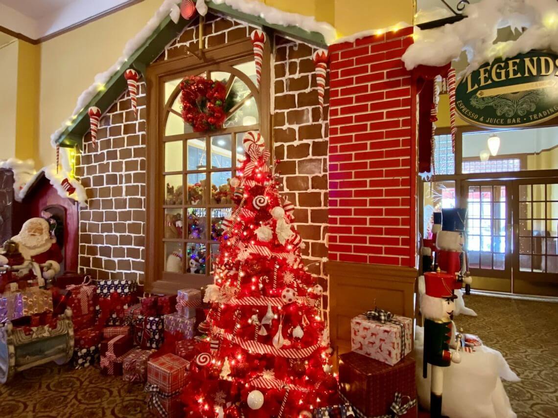 A festive Christmas display features a gingerbread house with candy cane decorations. A red and white themed Christmas tree is adorned with lights and ornaments. Wrapped gifts and a Santa figurine are nearby, creating a holiday ambiance.